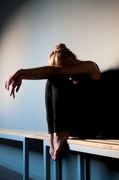 a woman sitting on top of a wooden bench next to a wall with her hands behind her head