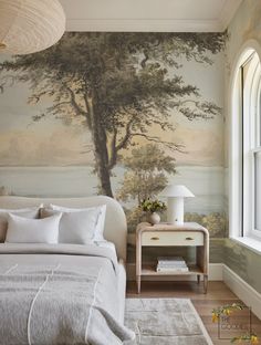 a bedroom with a tree mural on the wall next to a white bed and nightstand