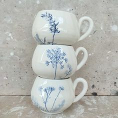 three coffee mugs with blue flowers on them sitting next to each other in front of a wall