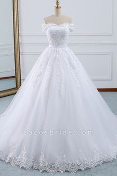 a white wedding dress on a mannequin in front of a gold framed mirror