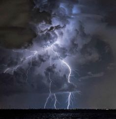 a large cloud filled with lots of lightning in the night sky over some water and land