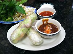 some food is on a white plate near bowls of soup and sauces with chopsticks