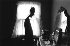 a man standing in front of a window next to a dresser