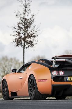 an orange sports car is parked on the side of the road in front of a tree