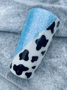 a blue and white cow print pillow sitting on top of a gray fuzzy fabric covered in glitter