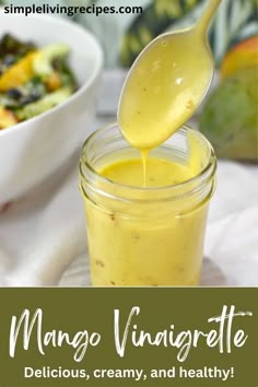 a spoon full of mango vinaigrete next to a bowl of fruit and vegetables