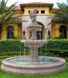 a water fountain in front of a house with palm trees and bushes around the perimeter