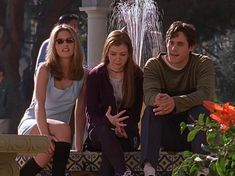 three people sitting on a bench in front of a fountain