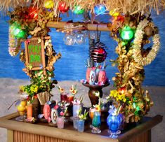 an outdoor bar decorated with flowers, candles and other decorations on the table in front of a tiki hut