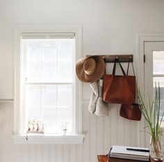 a hat and purse hanging on the wall next to a window in a white room