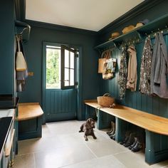 a dog is sitting on the floor in front of a bench and coat rack with coats