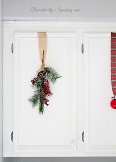 a christmas wreath hangs on the front door with red ornaments hanging from it's hooks