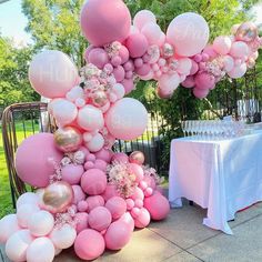 pink and white balloons are on display in front of a table at an outdoor party