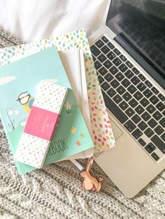 an open laptop computer sitting on top of a bed next to notebooks and books