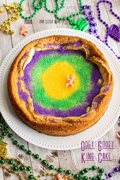 a colorful cake on a white plate surrounded by beads and necklaces with the words oddy gooey king cake