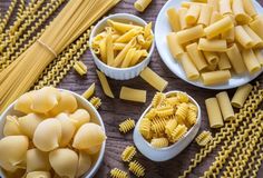 three bowls filled with different types of pasta on top of a wooden table next to two plates