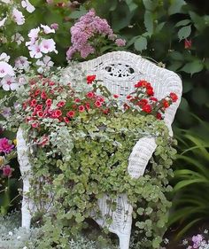 a white wicker chair covered in flowers and greenery next to a garden bed