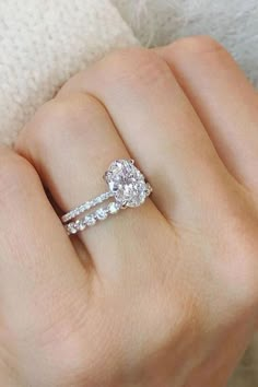 a woman's hand with two engagement rings on her finger and the ring has an oval