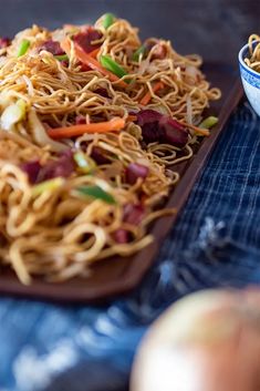 a plate of noodles and vegetables on a blue table cloth next to an onion dish