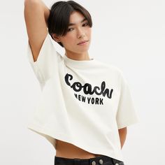 Detailed with our cursive Coach script this cropped T-shirt is crafted of soft cotton. The boxy silhouette features a comfortable easy to wear dropped shoulder. | Coach Cursive Signature Cropped T-Shirt - Women's Size Small - Cream Casual T-shirt With Logo Lettering For Spring, Spring Casual T-shirt With Logo Lettering, Casual Spring T-shirt With Logo Lettering, Summer Cotton Tops With Logo Lettering, Cotton Tops With Logo Lettering For Summer, Cotton Summer Tops With Logo Lettering, Casual Summer Tops With Logo Lettering, Trendy Boxy Cropped T-shirt With Crew Neck, Boxy Fit Logo Print Top