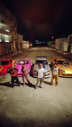 four people standing in front of three parked cars