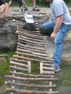 a man kneeling down next to a wooden bridge made out of sticks and logs in the water