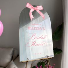 a bridal shower sign with a pink bow on it and balloons in the background