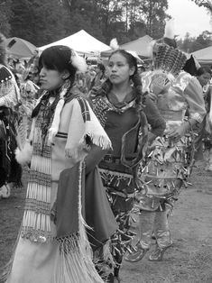 two women dressed in native american clothing standing next to each other at an outdoor event