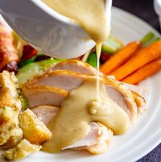 a person pouring gravy on top of a plate of food with carrots