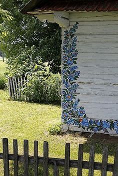 an old white house with blue flowers painted on it's side next to a wooden fence