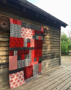 a red and black patchwork quilt hanging on the side of a wooden cabin wall