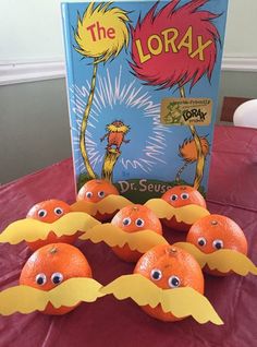 oranges with googly eyes are sitting on a table next to an open book