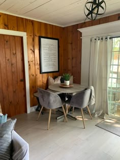 a living room with wood paneled walls and wooden flooring, two chairs at a round table in front of a sliding glass door