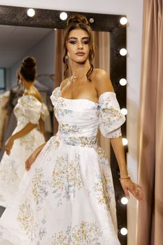 a woman standing in front of a mirror wearing a white dress with flowers on it