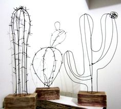 three metal cactus sculptures sitting on top of a wooden table next to a white wall