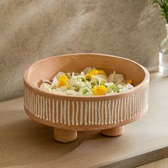 a wooden bowl filled with food on top of a table next to a vase full of flowers