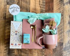 a pink box filled with lots of items on top of a wooden table next to a cup