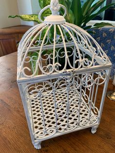 a white birdcage sitting on top of a table next to a potted plant