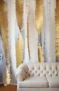 a white couch sitting in front of a wall with gold and silver foil on it