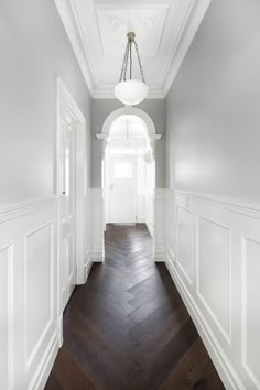 an empty hallway with white walls and wood flooring on the other side is a chandelier