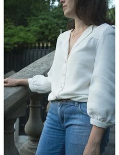 a woman leaning on a railing with her hands in her pockets and looking off into the distance