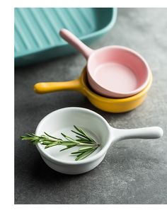 three bowls and spoons are sitting on the table with rosemary sprigs in them