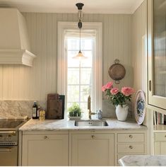 a kitchen with marble counter tops and white cabinets, along with pink flowers on the window sill