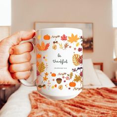 a person holding a coffee mug with the words be grateful on it in front of a bed