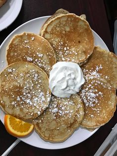 pancakes on a plate with whipped cream and orange slices