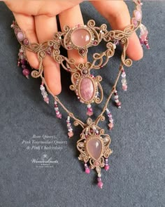 a woman's hand holding an elaborate necklace with pink stones and beads on it