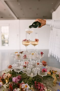 a person pouring champagne into wine glasses on top of a table with flowers and greenery