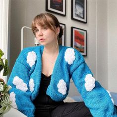 a woman sitting on top of a bed wearing a blue sweater with white flowers in it