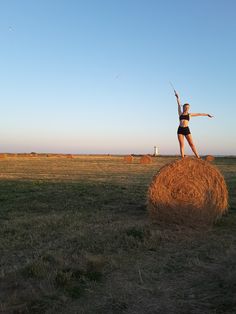 a woman standing on top of a hay bale in the middle of a field