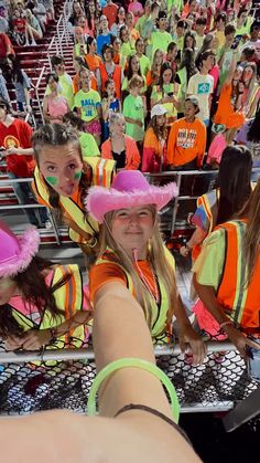 a group of girls in neon colored outfits and pink hats at a sporting event with people watching